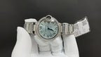 Cartier watch on wristband with open clasp, Roman numeral dial, and diamond bezel.