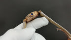 Gold-tone wristwatch with blue gem bezel and cream leather strap, angled view