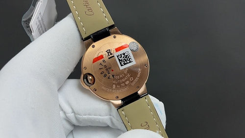 Cartier watch case back with visible movement and QR code, rose-gold finish, black strap