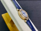 Cartier watch on stand with blue leather strap, gold case, diamond bezel