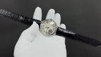 Wristwatch on black croc-texture leather strap, white dial on gloved hand