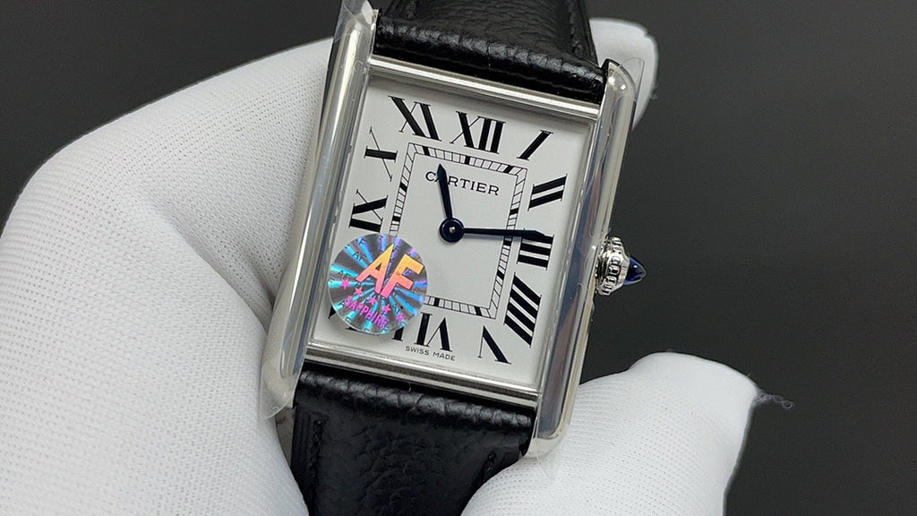 Cartier watch with black leather strap, silver case, white Roman numeral dial and blue gem.