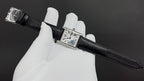 Cartier watch with black leather strap, rectangular silver case, and Roman numeral dial.