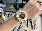 Digital wristwatch on wrist with translucent white strap and gold-tone bezel, round face