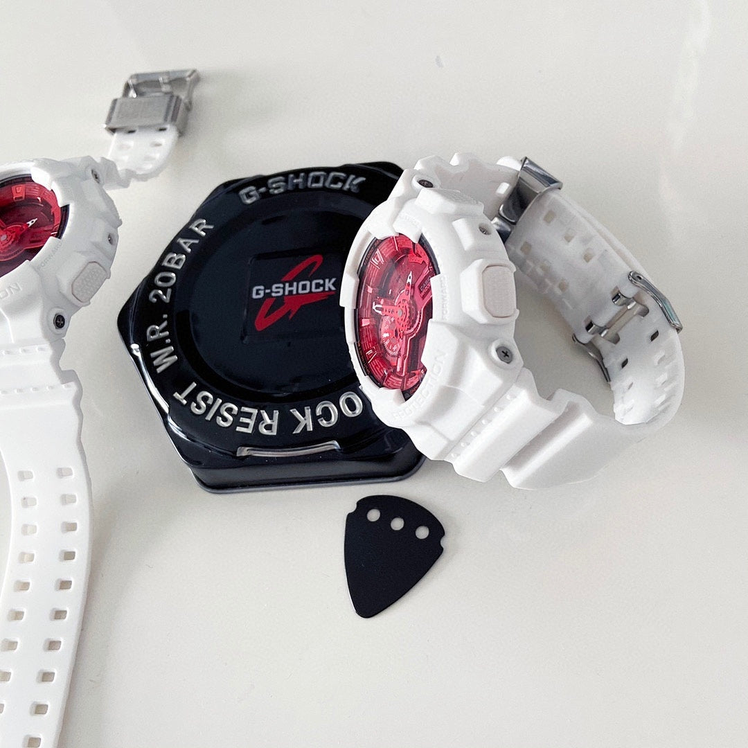 White resin wristwatch with red dial beside black G-Shock-style case and strap tag