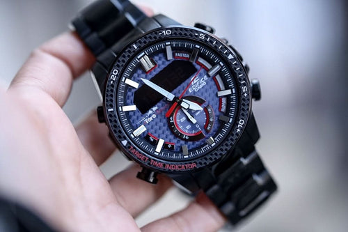 Black Casio watch with chronograph-style dial, red accents, black link bracelet.
