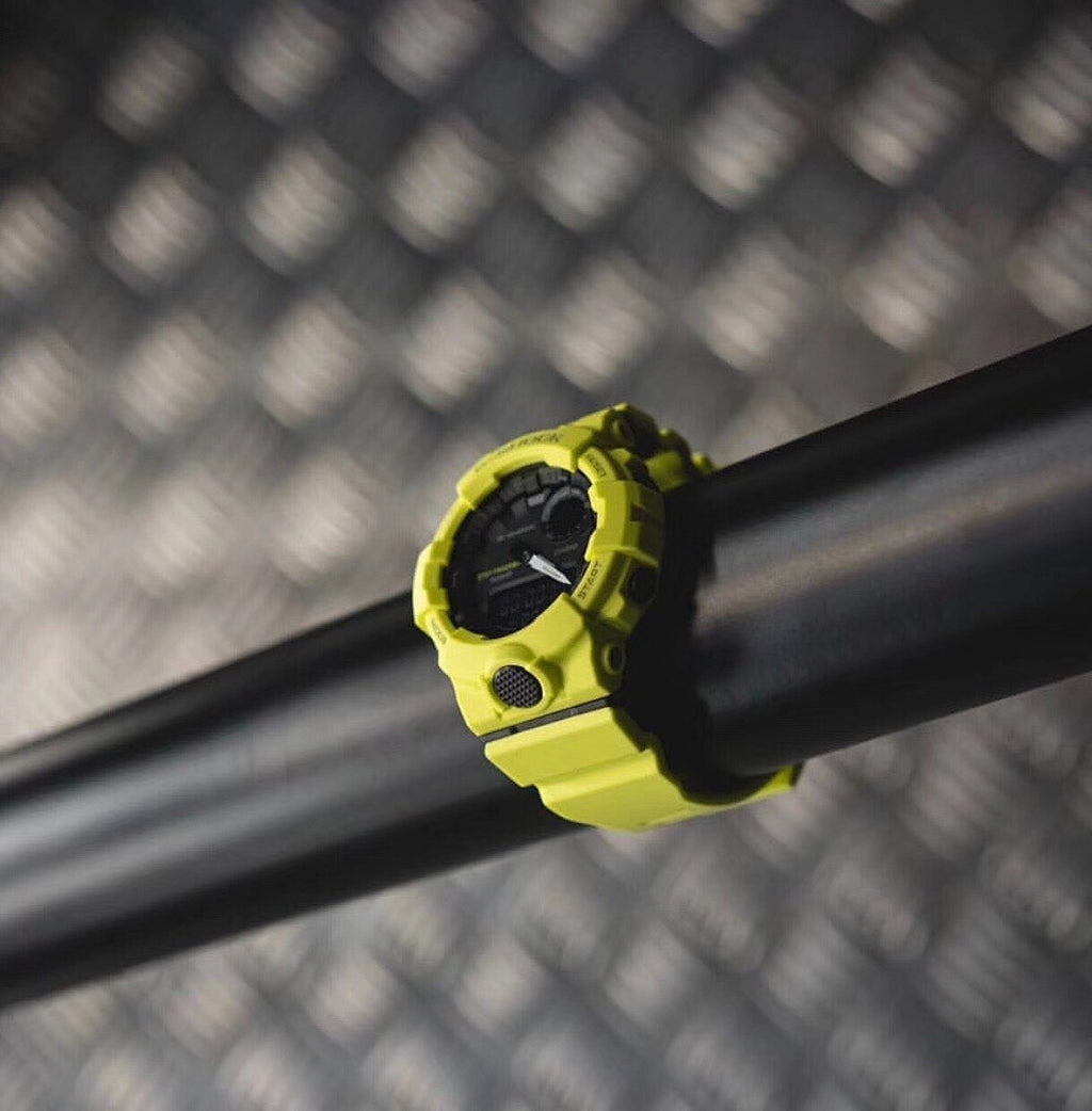 Casio watch with bright yellow strap and round digital face on a dark bar