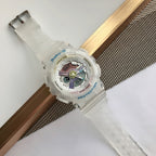 White resin Baby-G watch resting on wood rail, round multicolor dial visible