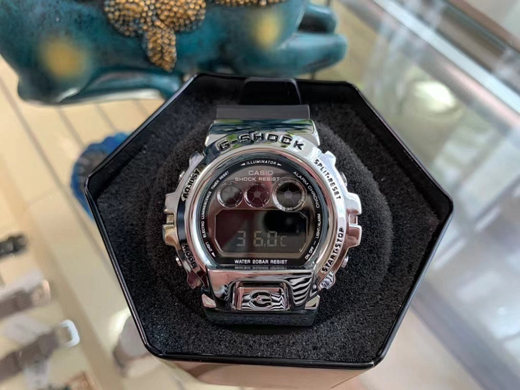 Silver digital G-Shock-style watch with LCD display and metal bezel, in box.