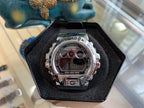 Silver digital G-Shock-style watch with LCD display and metal bezel, in box.