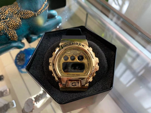 Gold digital G-Shock-style watch with black strap and LCD screen, in hex box.