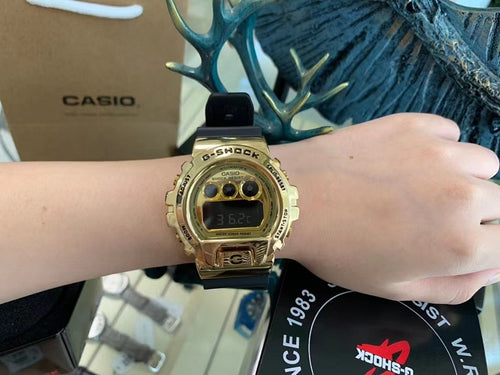 Gold digital G-Shock-style watch on wrist with LCD display and black strap.