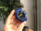 Casio G-Shock blue digital watch held in hand, black dial with yellow highlights