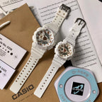 Casio watch pair with white resin straps and gold-toned multi-dial faces on cards