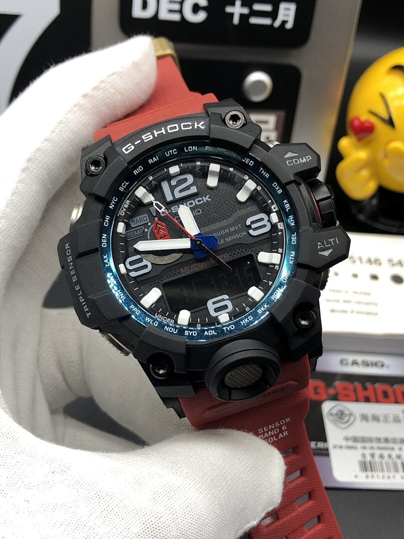 Casio G-Shock wristwatch with black case, red strap, and blue-accent bezel on hand
