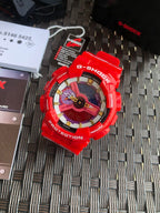 Red Casio G-Shock watch viewed from above, colorful dial on textured mat