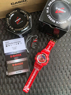 Casio G-Shock watch with red band and round dial, with retail boxes on mat