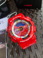 Red Casio G-Shock wristwatch, colorful dial with gold markers on textured mat