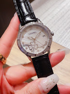 Chanel watch with black leather strap, white dial, diamond bezel, and flower motifs