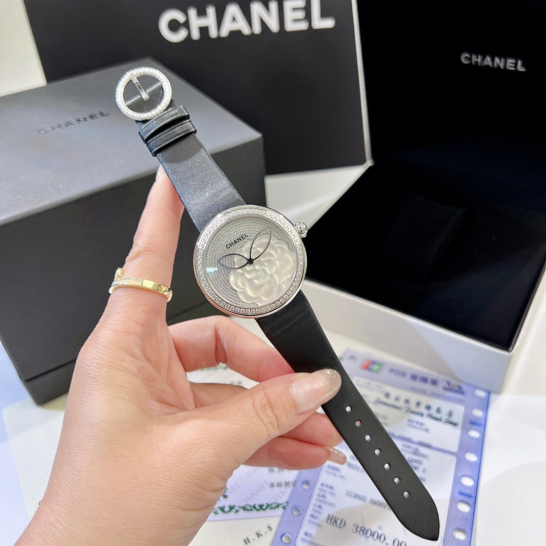 Chanel round wristwatch with black strap and silver-tone bezel held in hand