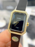 Chanel watch front: gold diamond bezel, black dial with CHANEL and SWISS, black strap
