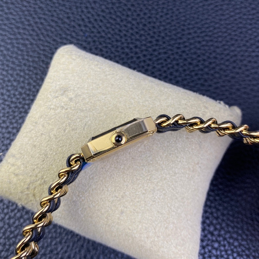 Gold-tone side of a watch case with small round detail on a navy blue chain bracelet
