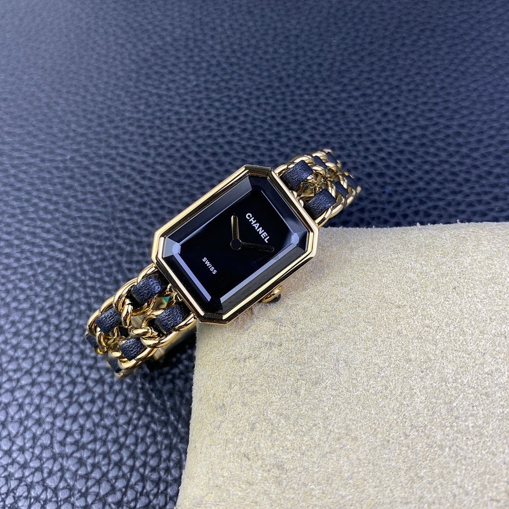Gold-tone rectangular watch with navy blue link bracelet and dark dial on cream cushion