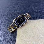 Gold-tone rectangular watch with navy blue link bracelet and dark dial on cream cushion