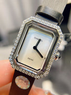Chanel watch with diamond-encrusted bezel, silver face, and black leather strap