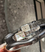 Rectangular wristwatch with silver-tone metal bracelet and light dial on a curved display