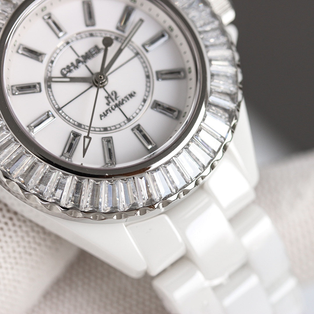 Chanel watch face with silver-tone jeweled bezel, white dial, baton markers and hands.