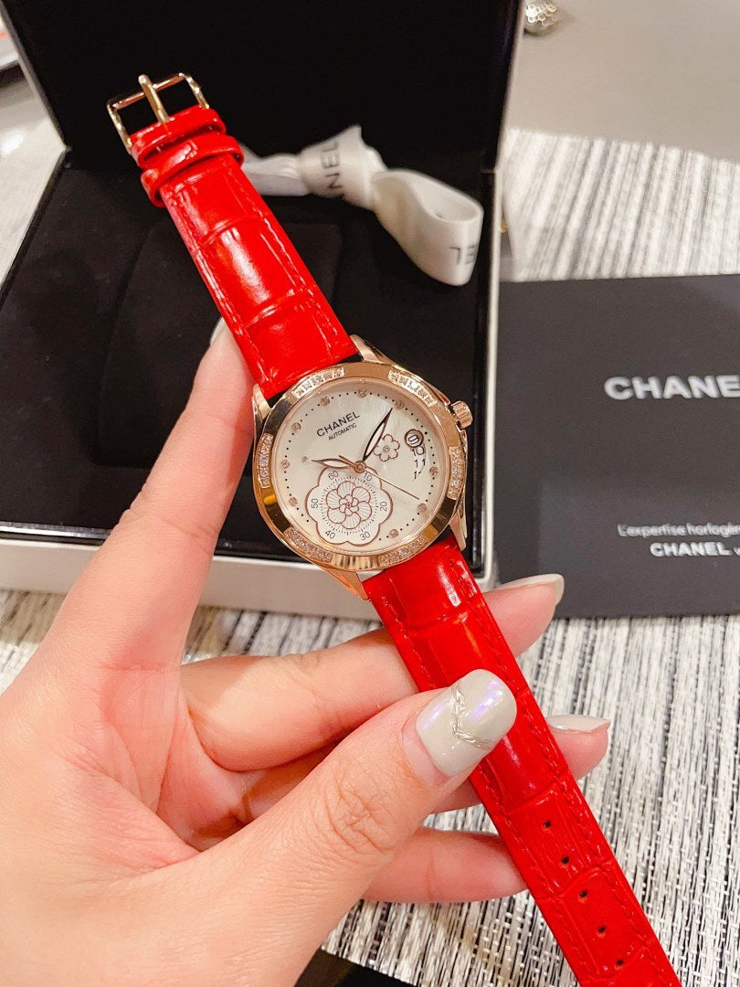 Chanel watch with red leather strap, gold-tone bezel and floral dial, held in hand