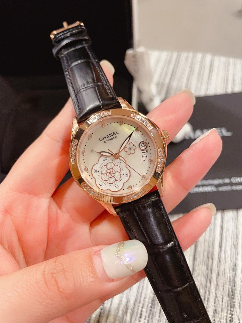 Chanel watch with black leather strap, round gold-tone case and floral dial on hand