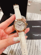 Chanel watch with white leather strap, gold-tone case and floral dial, held in hand