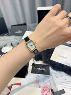 Gold-toned square wristwatch with light dial and black leather strap on wrist