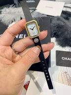 Close-up of gold-toned square wristwatch with light dial and black leather strap
