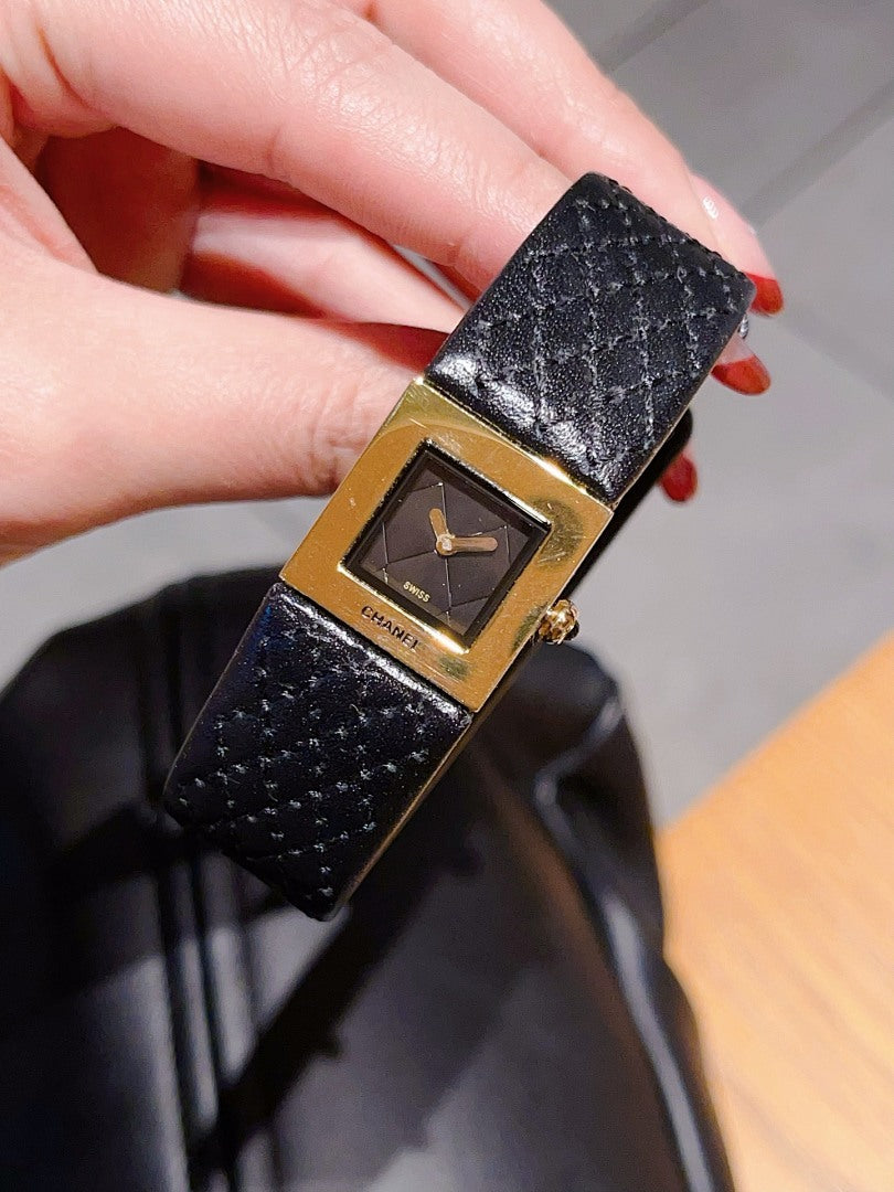 Chanel watch with black leather strap and gold-tone square dial on a hand