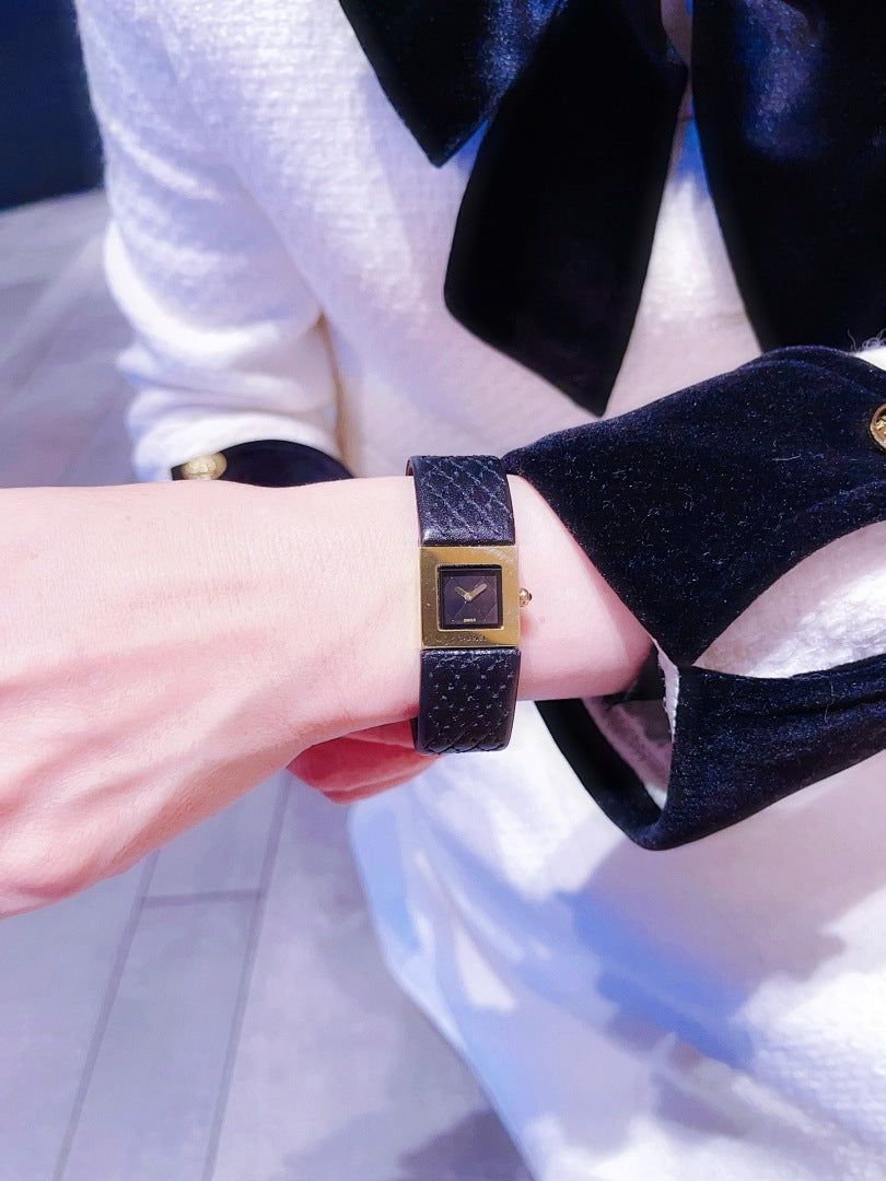 Chanel watch with black leather strap and gold-tone square face on a dressed wrist