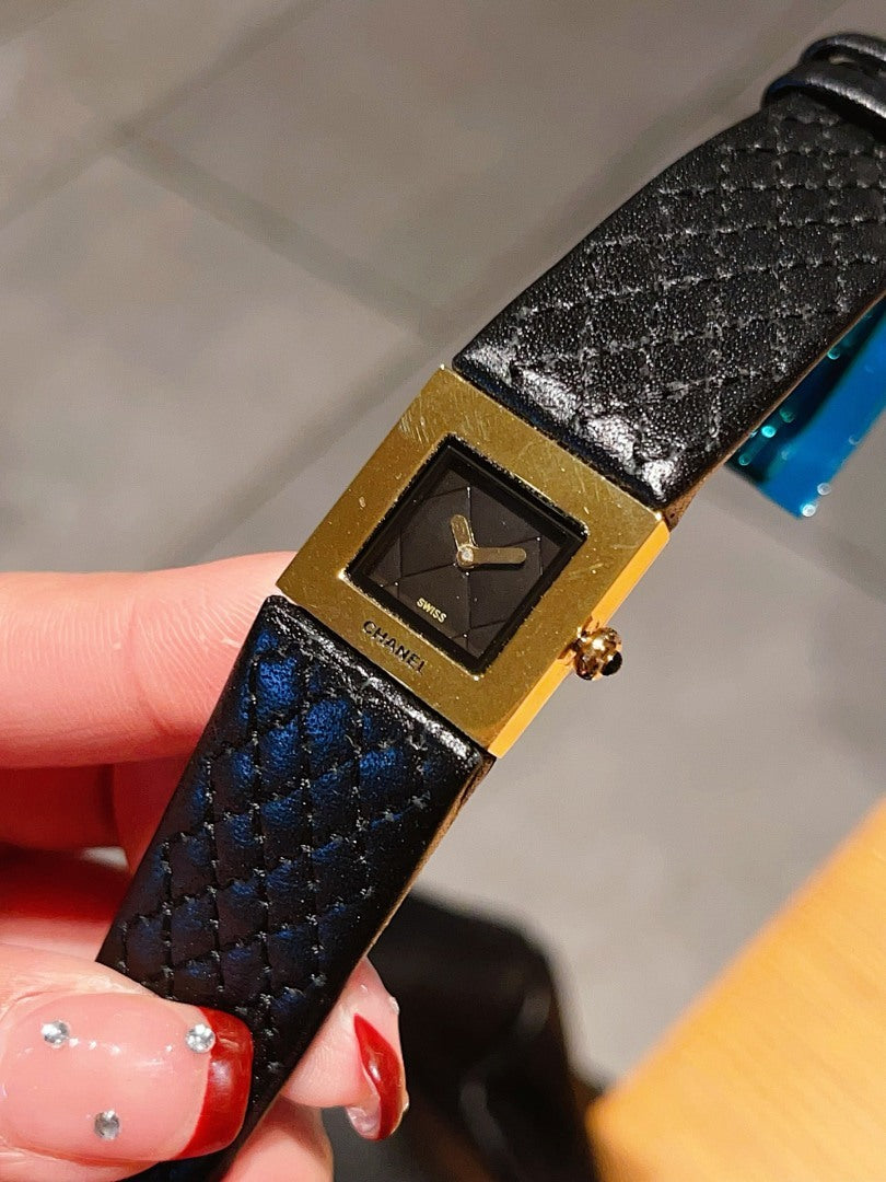 Chanel watch close-up with black textured leather strap and gold-tone square dial