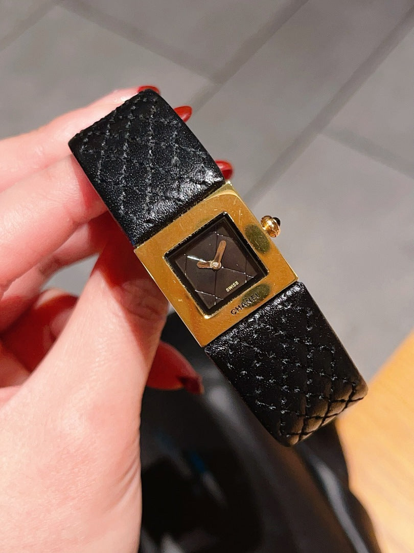 Chanel watch held in hand with black leather strap and gold-tone square dial