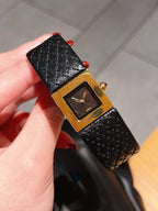 Chanel watch held in hand with black leather strap and gold-tone square dial