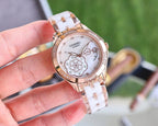 Gold-tone Chanel watch on white bracelet strap, round white dial and jeweled bezel