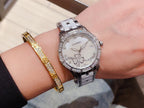 Chanel wristwatch on wrist with white floral dial, jeweled bezel, and silver metal link strap.