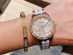 Chanel wristwatch with white floral dial, rose gold tone bezel, and silver metal link strap.