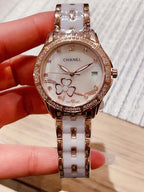 Chanel wristwatch with white floral dial, rose gold tone bezel, and silver metal link strap.