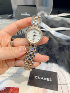 Chanel watch held in hand, round silver dial with gold-tone bracelet