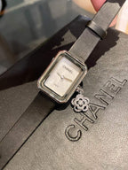 Chanel watch with square silver case, white dial, and black leather strap with charm
