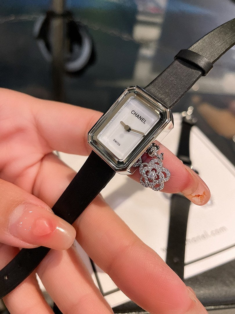 Chanel watch with square silver case, black dial, and black leather strap with dangling charm