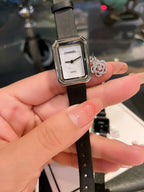 Chanel watch with square silver case, white dial, and black leather strap being held