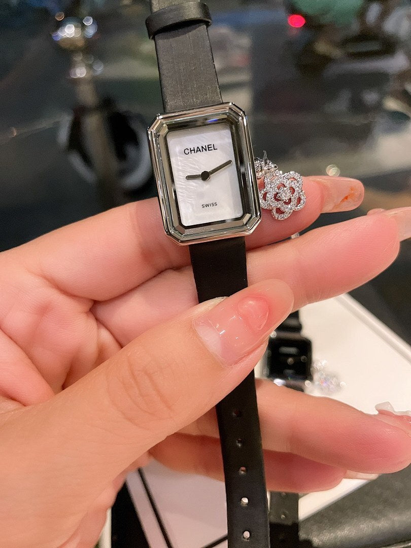 Chanel watch with square silver case, white dial, and black leather strap being held